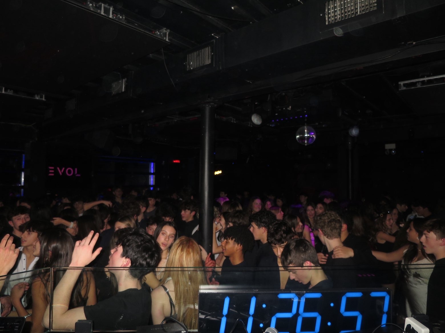 Packed dance floor at EVOL — disco ball spinning above a crowd lit in blue and purple, countdown clock glowing in the foreground.